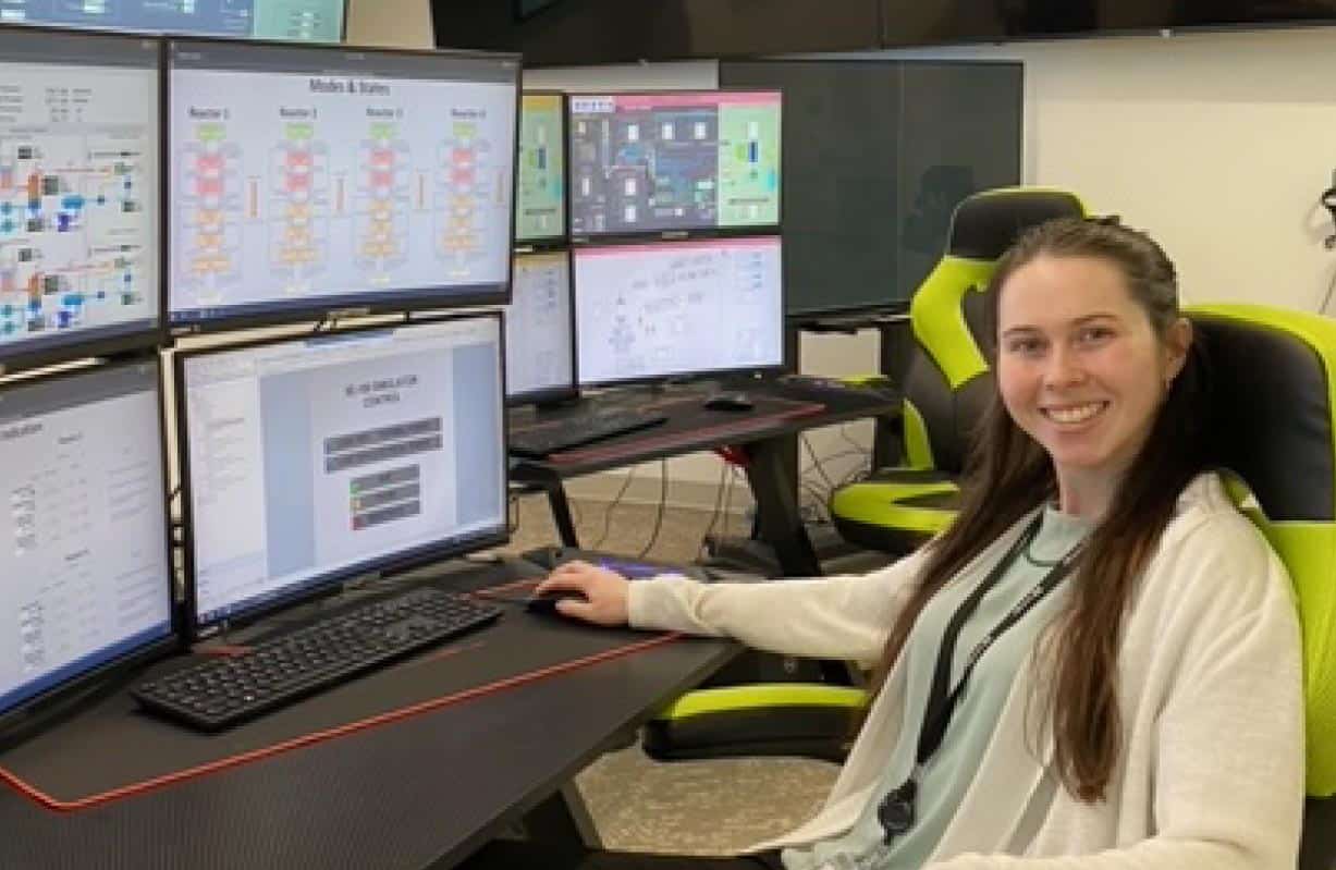 woman sits in chair in front of multiple monitors