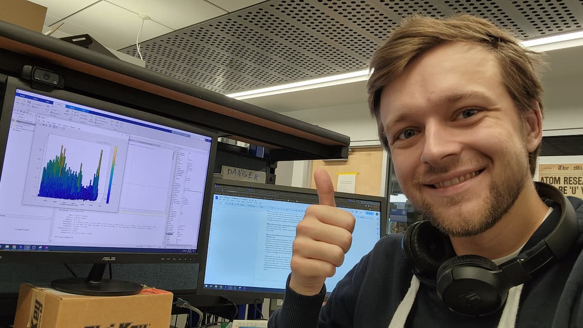 a man sitting in front of two computer screens and giving the thumbs up