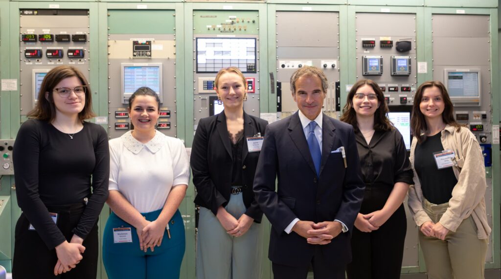 six people standing in front of a wall of knobs, dials and computers