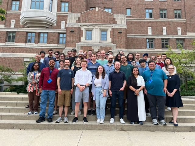 a large group of students gathers on a staircase in front of a large brick building